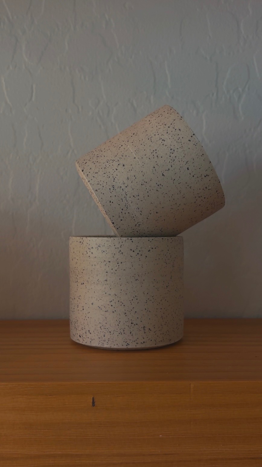 Two light speckled ceramic cups stacked at an angle